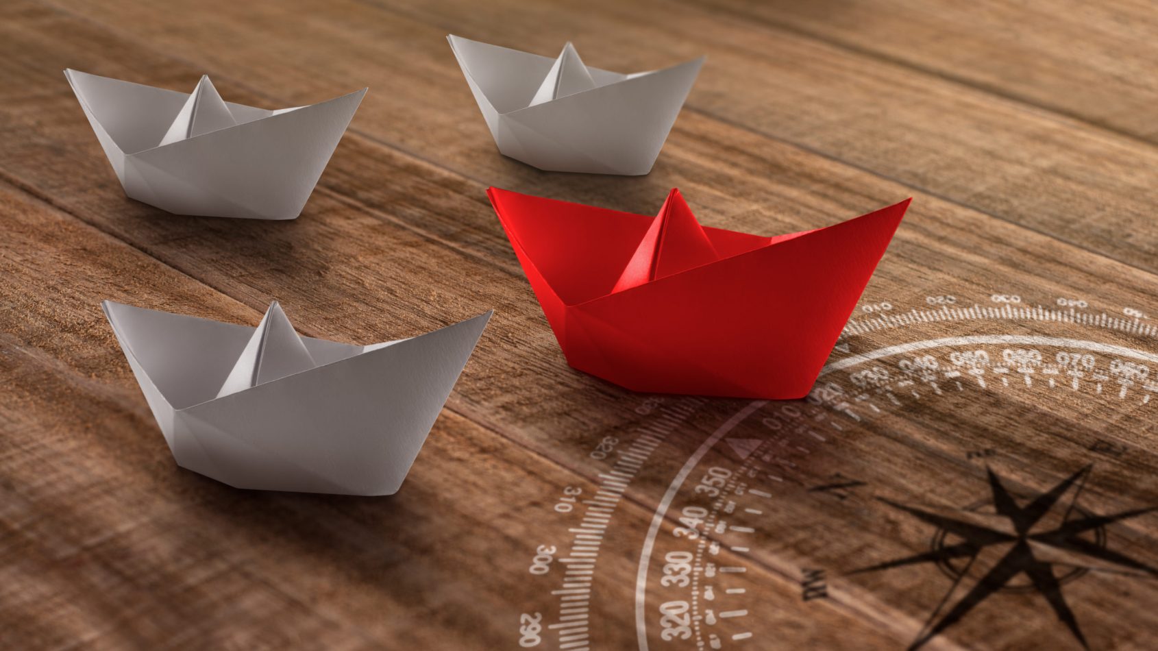 Leadership concept with red paper ship leading among the white on a rustic wooden background. Business, travel, or shipping industry concept.